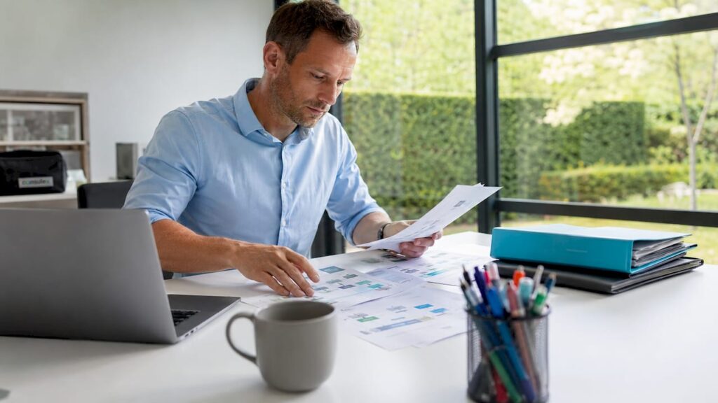 Een man zit aan zijn bureau en werkt geconcentreerd aan het ordenen van workflow-schema’s.
