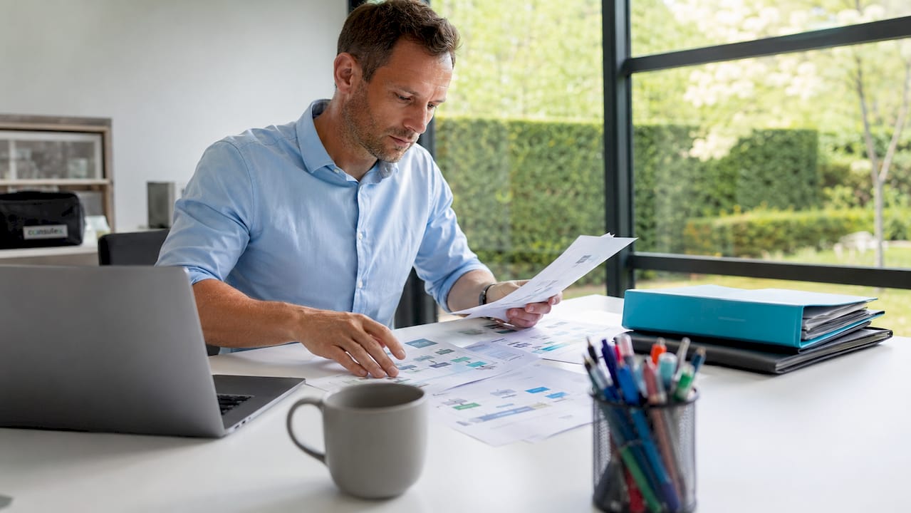 Een man zit aan zijn bureau en werkt geconcentreerd aan het ordenen van workflow-schema’s.